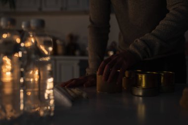 Önplandaki bulanık su ve konserve yiyecek stoğunun yanında bir adamın kısmi görüntüsü