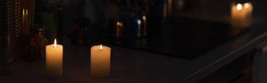 candles burning on kitchen worktop in darkness during energy blackout, banner clipart