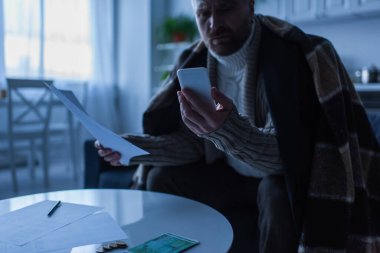 Alacakaranlıkta masanın yanındaki akıllı telefona bakan donmuş bir adam.