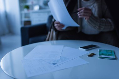 Paranın yanında ödeme faturaları olan bir adamın kısmi görüntüsü ve enerji kesintisi sırasında boş ekranlı akıllı telefon