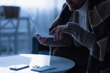 Alacakaranlıkta paranın ve akıllı telefonun yanında ödemeleri tutan donmuş adamın kısmi görüntüsü