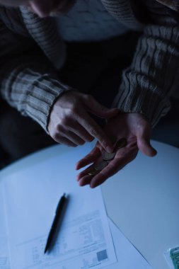 Elektrik kesintisi sırasında bulanık ödeme faturalarının yakınındaki madeni paraları sayan adamın kısmi görüntüsü