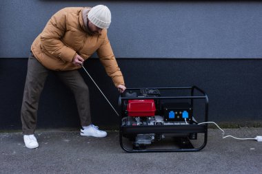 Kapalı ceketli adam elektrik kesintisi sırasında güç jeneratörünü çalıştırıyor.