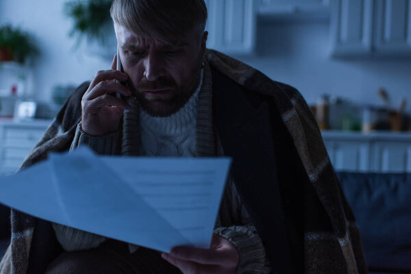 напряженный человек разговаривает по мобильному телефону, глядя на счета за оплату во время отключения электроэнергии