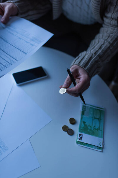 KYIV, UKRAINE - NOVEMBER 2, 2022: cropped view of man holding coin and payment bills near smartphone and euro banknotes