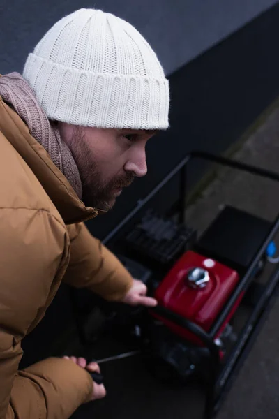 Mann Mit Strickmütze Schaut Weg Während Stromgenerator Auf Verschwommenem Hintergrund — Stockfoto