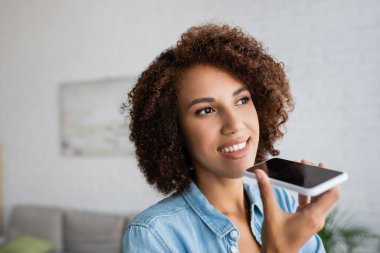 Kıvırcık saçlı neşeli Afrikalı Amerikalı kadın akıllı telefondan sesli mesaj kaydediyor. 