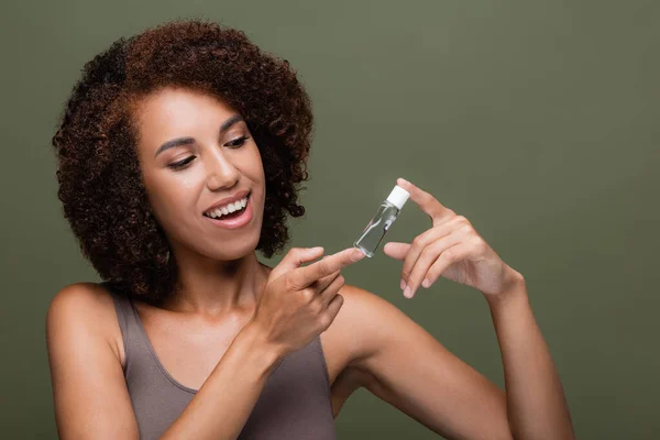 アフリカ系アメリカ人の女性が緑色に孤立した化粧品油のボトルを見て微笑む — ストック写真