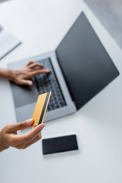 Обрезанный вид африканской американки, держащей кредитную карту и использующей ноутбук с чистым экраном дома 