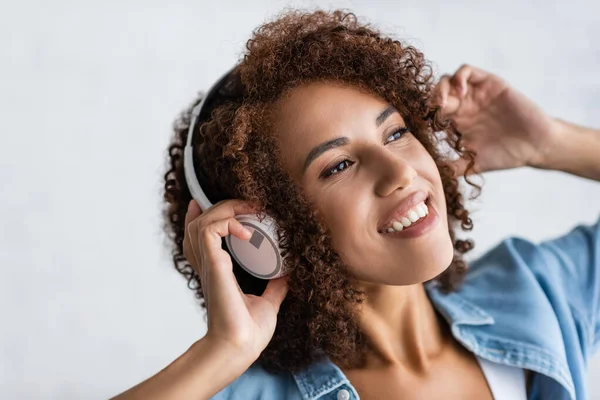 ワイヤレスヘッドフォンで音楽を聴きながら笑う幸せなアフリカ系アメリカ人女性 — ストック写真