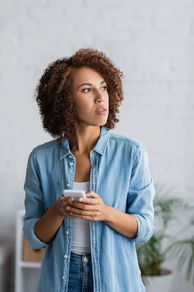 Curly African American Woman Holding Smartphone Looking Away Home — Stock Photo, Image