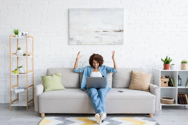 ソファに座って家で働いている間にラップトップを使って興奮したアフリカ系アメリカ人女性 — ストック写真