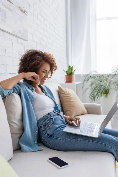 ソファに座って家で仕事をしながらノートパソコンを使うアフリカ系アメリカ人の女性 — ストック写真
