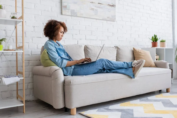 ソファに座って自宅で仕事をしながらノートパソコンを使うアフリカ系アメリカ人女性に焦点を当て — ストック写真
