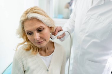 Doktor orta yaşlı bir kadının boynundaki lenf düğümlerinin ultrasonunu yapıyor.