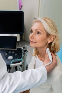 Doktorun yanında gülümseyen sarışın kadın klinikte lenf düğümlerinin ultrasonunu çekiyor.