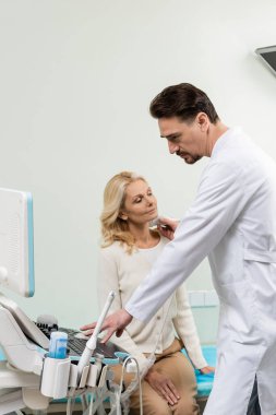 Ciddi bir doktor, olgun bir kadının teşhisini yaparken ultrason makinesi kullanıyor.
