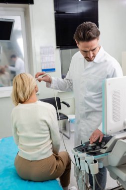 Beyaz önlüklü bir doktor orta yaşlı bir kadını teşhis ederken ultrason cihazını ayarlıyor.