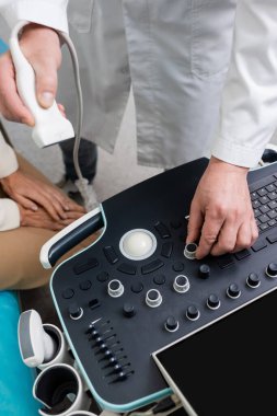 partial view of physician adjusting ultrasound machine near patient in hospital clipart