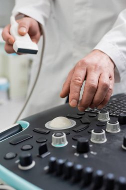 partial view of blurred doctor holding probe while using ultrasound machine clipart