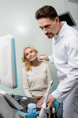 Doktor sarışın kadının teşhisi sırasında ultrason cihazına bakıyor.