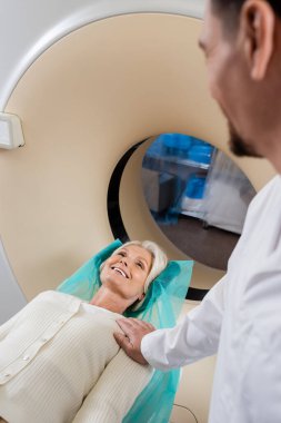 Klinikteki bilgisayarlı tomografi sırasında gülümseyen kadını sakinleştiren bulanık radyoloji uzmanı.