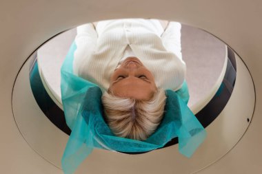 pretty blonde woman with closed eyes doing examination on computed tomography scanner clipart