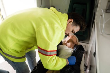 Paramedic in uniform taking off jacket from unconscious patient in emergency car  clipart