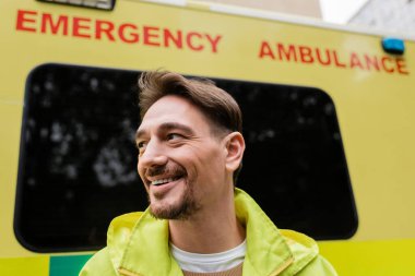 Bulanık ambulans arabasının yanında duran olumlu sağlık görevlisinin portresi. 