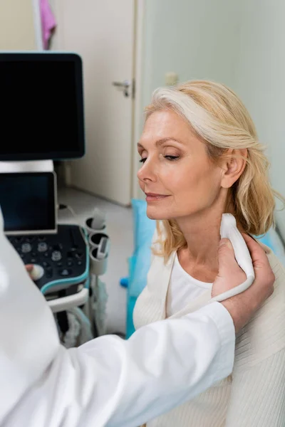 blonde middle aged woman near doctor doing ultrasound of her neck in clinic