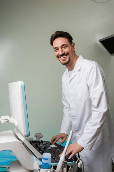 Szczęśliwy Lekarz Białym Płaszczu Patrząc Kamerę Podczas Obsługi Ultradźwięków Klinice — Zdjęcie stockowe