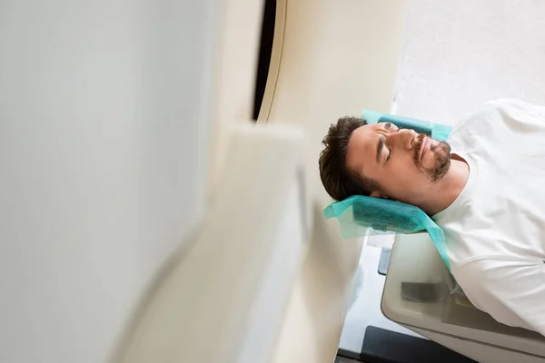 診療所のCtスキャナの検査中に目を閉じたままの心配な男 — ストック写真