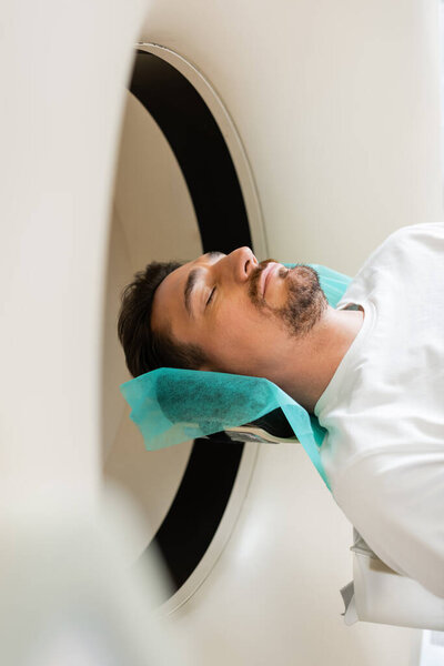 bearded man with closed eyes lying during diagnostics on computed tomography machine
