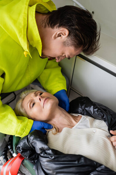 High angle view of paramedic checking neck of middle aged patient in emergency vehicle 