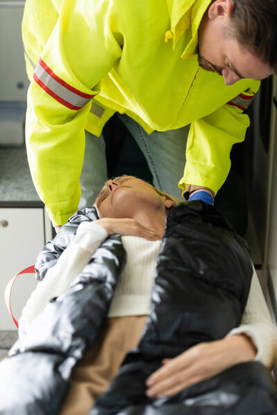 Paramedic in uniform giving first aid to middle aged patient in emergency vehicle 