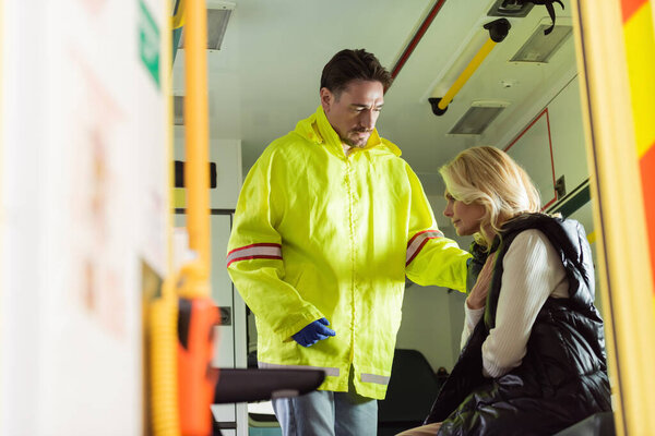 Paramedic in uniform calming middle aged woman in emergency car 