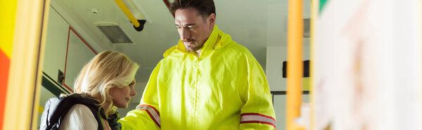 Paramedic in uniform looking at sick woman in emergency car, banner 