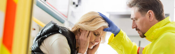 Paramedic in latex glove touching head of sick woman in emergency car, banner 