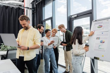 Çok ırklı iş adamları ellerinde aletler ve kahveyle toplantı odasına gidiyorlar.