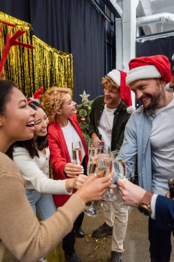 Noel Baba şapkalı çok ırklı iş adamları Noel 'i ofiste kutlarken ellerinde şampanya tutuyorlar. 