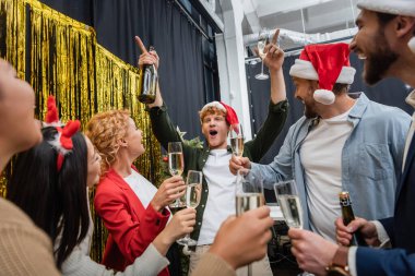 Noel Baba şapkalı heyecanlı işadamı, Noel 'i çok ırklı meslektaşlarıyla kutlarken şampanya tutuyor. 