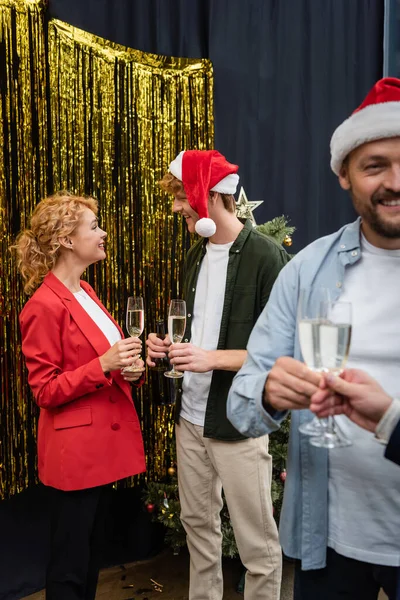 オフィスでクリスマスパーティー中にチンセルの近くで話してシャンパンのグラスを持つ笑顔ビジネスの人々 — ストック写真