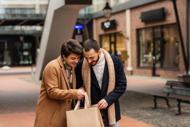 Moda kıyafetli mutlu eşcinsel çift Bulanık sokakta alışveriş torbalarına bakıyor