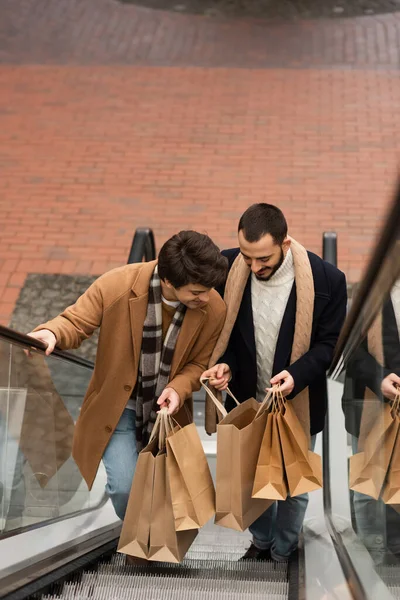 Yüksek Açılı Şık Mutlu Eşcinseller Yürüyen Merdivende Alışveriş Torbalarına Bakıyorlar — Stok fotoğraf