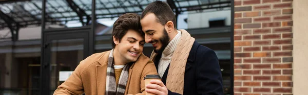喜ばしい髭を生やした男がコーヒーを持って街のゲイのパートナーの近くに行き — ストック写真