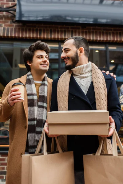 快乐的同性恋夫妇穿着时髦的衣服 站在一边 一边买东西一边喝着外卖 — 图库照片