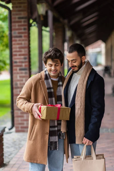 年轻快乐的基佬拿着圣诞礼物站在时髦的男朋友旁边 提着购物袋 — 图库照片
