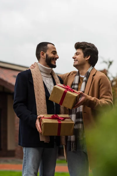 トレンディーで陽気なゲイの男性とクリスマスプレゼントお互いを見ます上のぼやけた前景 — ストック写真