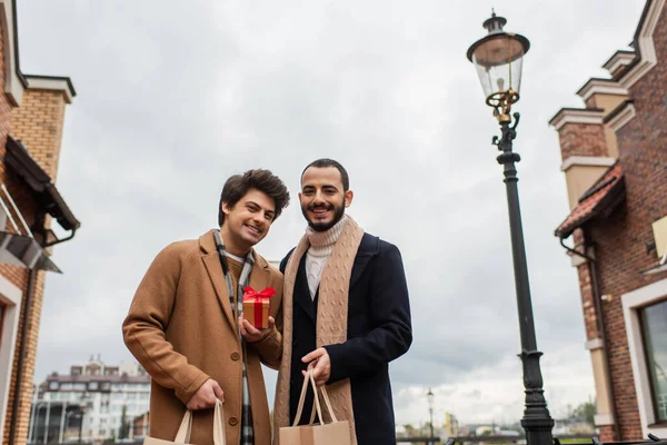 Fröhliches Und Stilvolles Homosexuelles Paar Mit Einkaufstaschen Und Kleiner Geschenkschachtel — Stockfoto