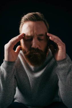 Tensed bearded man in jumper touching head isolated on black with shadow  clipart